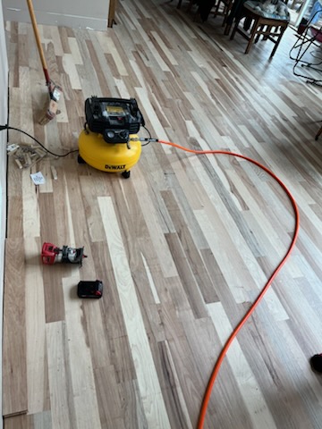 Unfinished hardwood planks mid-install with an air compressor and tools
